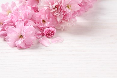 Photo of Beautiful sakura tree blossoms on white wooden table, closeup. Space for text