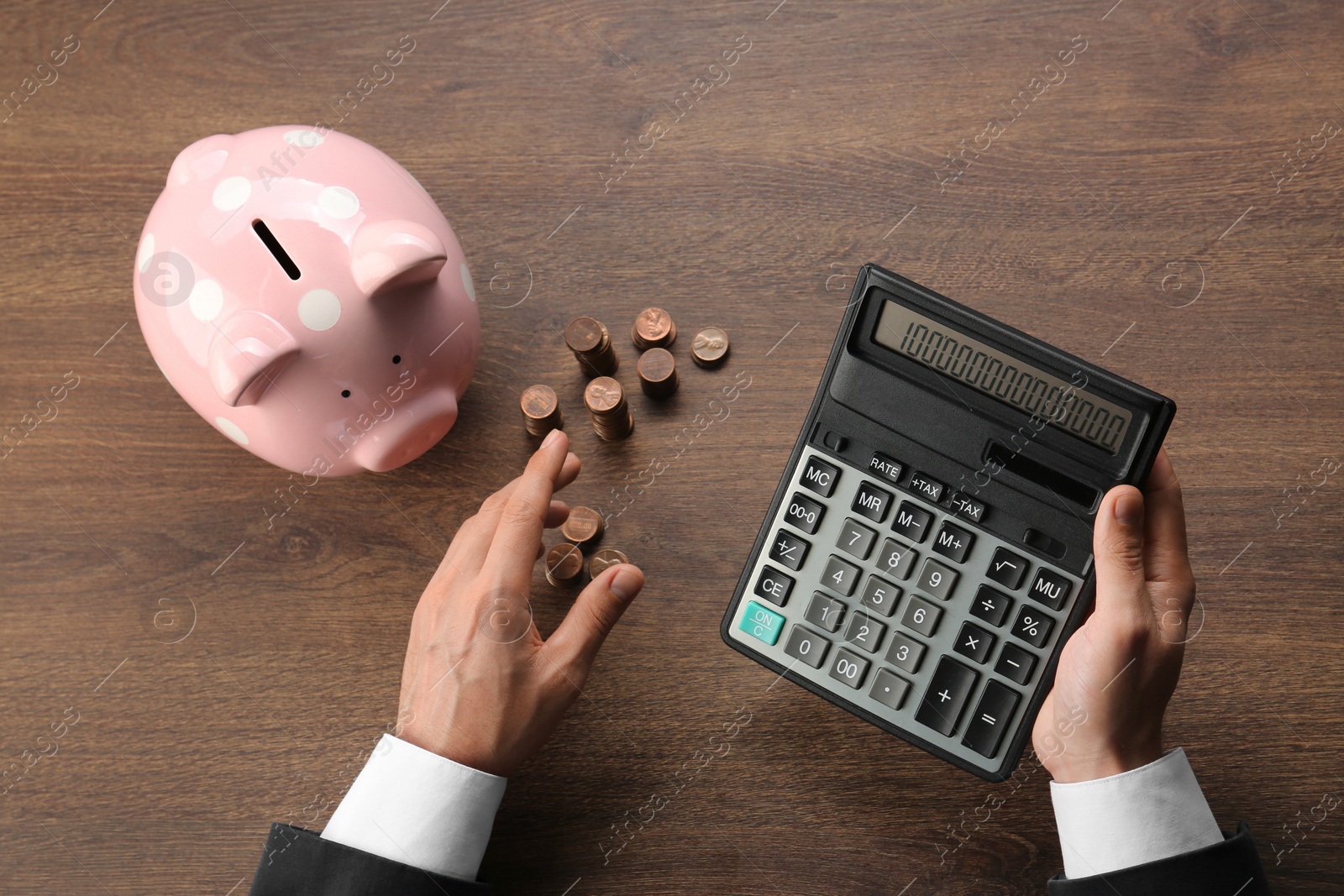 Photo of Budget planning. Businessman with piggy bank calculating at wooden table, top view