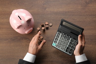 Photo of Budget planning. Businessman with piggy bank calculating at wooden table, top view