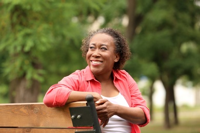 Portrait of happy African-American woman on bench in park