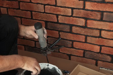 Photo of Professional builder filling fugue with grout gun near brick wall, closeup. Tiles installation process