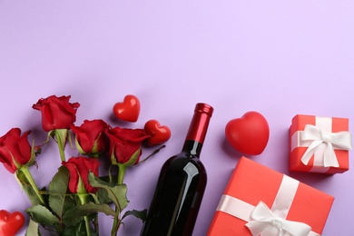 Photo of Flat lay composition with beautiful red roses and bottle of wine on violet background, space for text. Valentine's Day celebration
