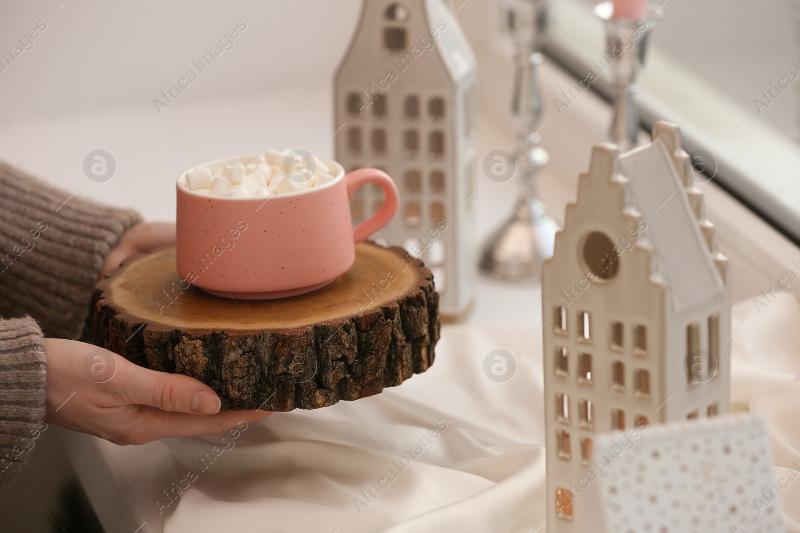 Photo of Woman holding cup of delicious drink near windowsill with house shaped lanterns indoors, closeup. Space for text