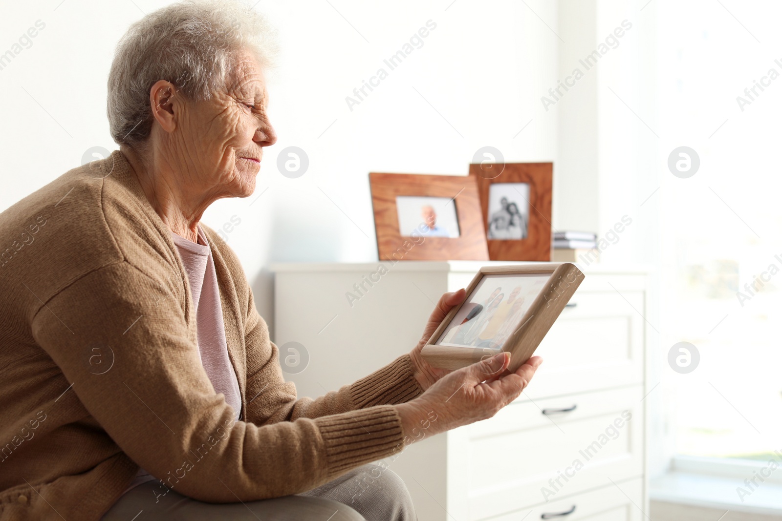Photo of Elderly woman with framed family portrait at home