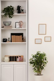 Photo of Stylish shelves with decorative elements and houseplants near white wall. Interior design