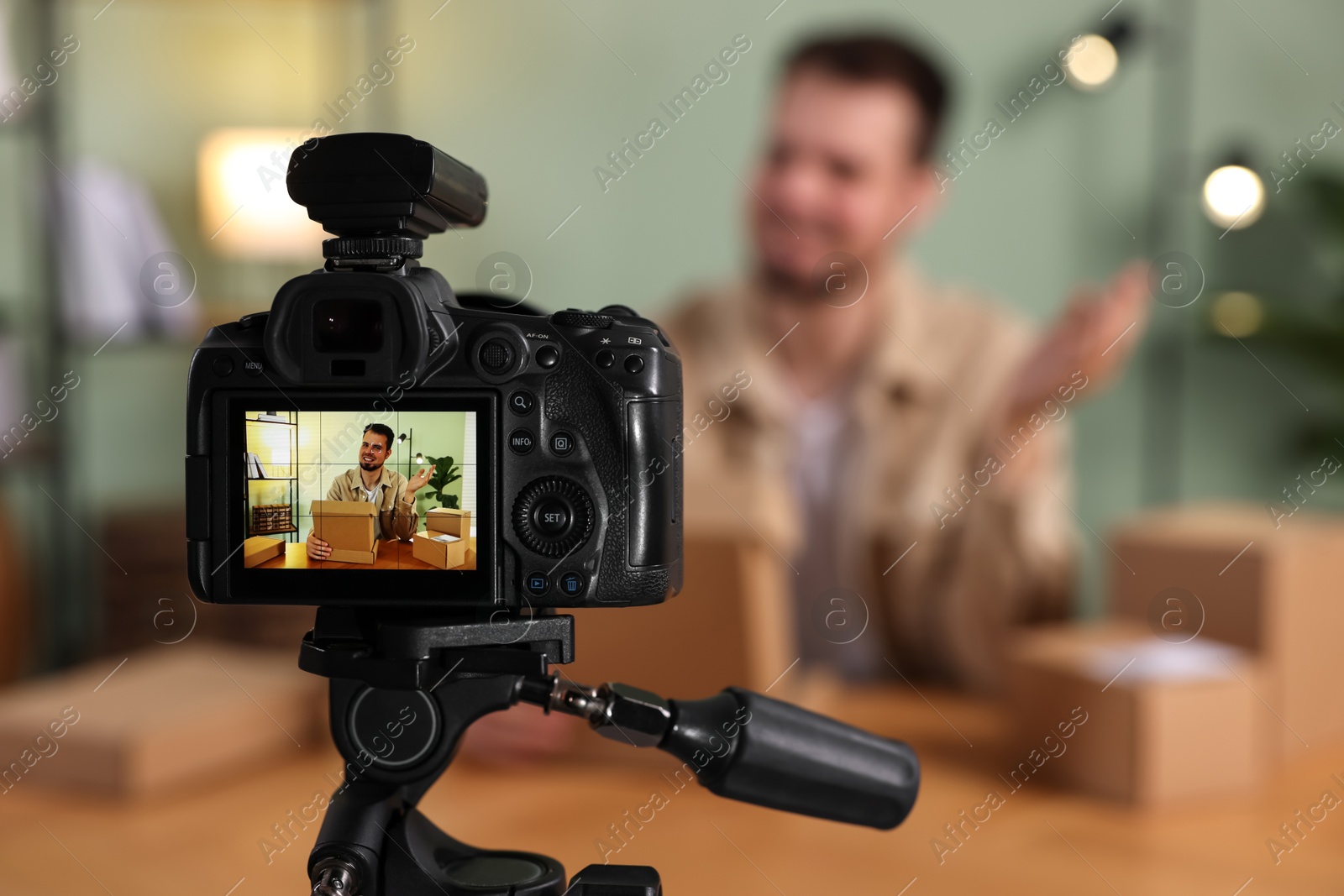 Photo of Blogger with many parcels recording video at home, focus on camera