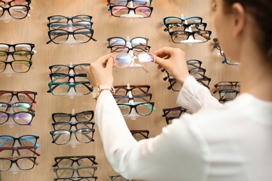 Photo of Female ophthalmologist taking glasses from showcase in optical store