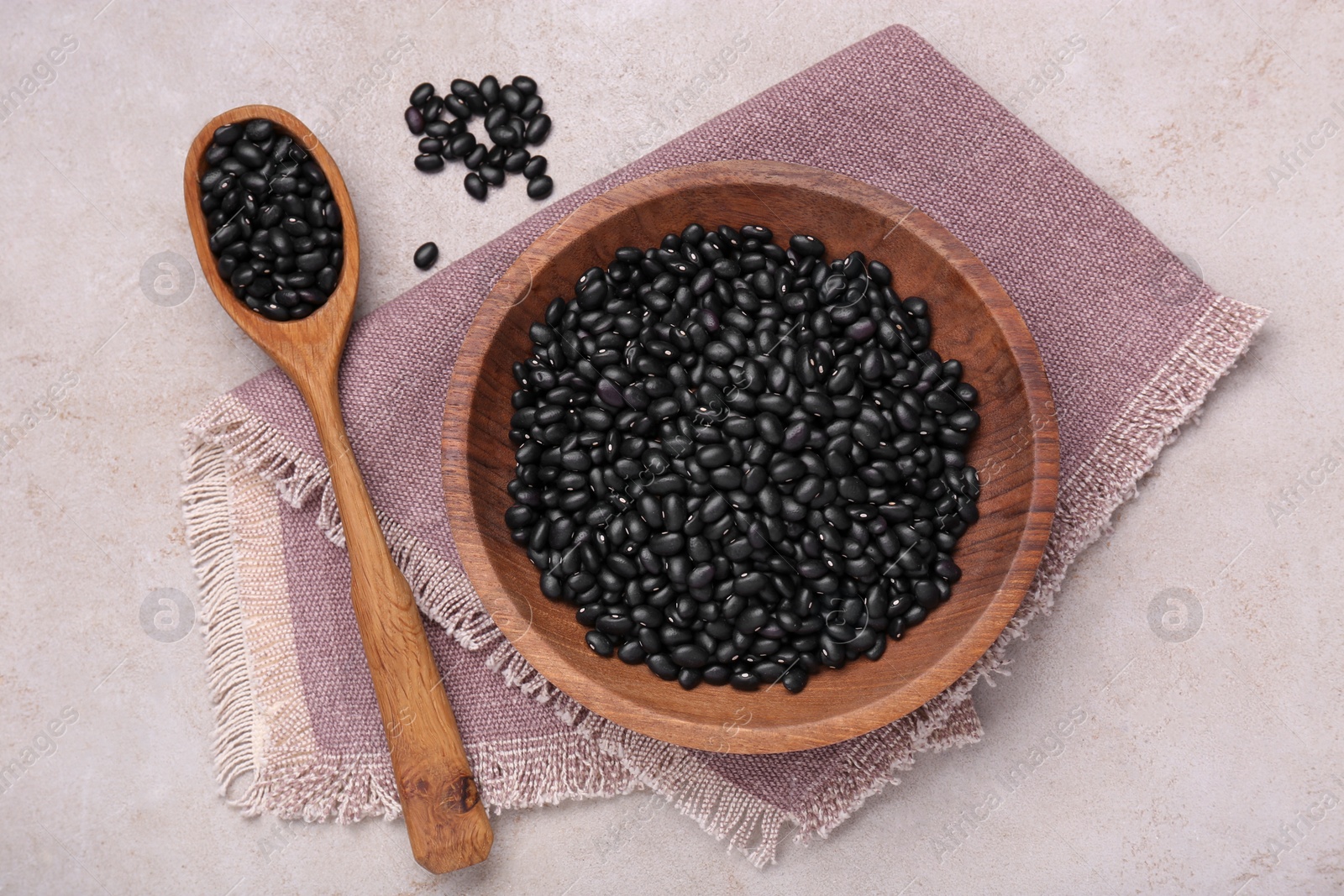 Photo of Bowl and spoon of raw black beans on light grey table, flat lay