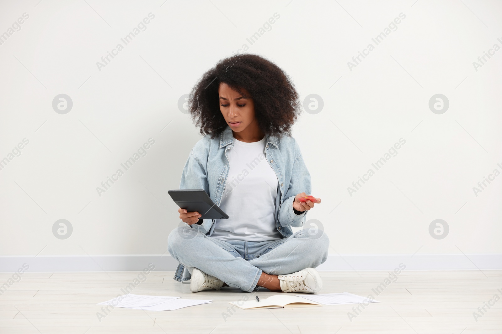 Photo of Confused woman with credit card and calculator planning budget indoors. Debt problem