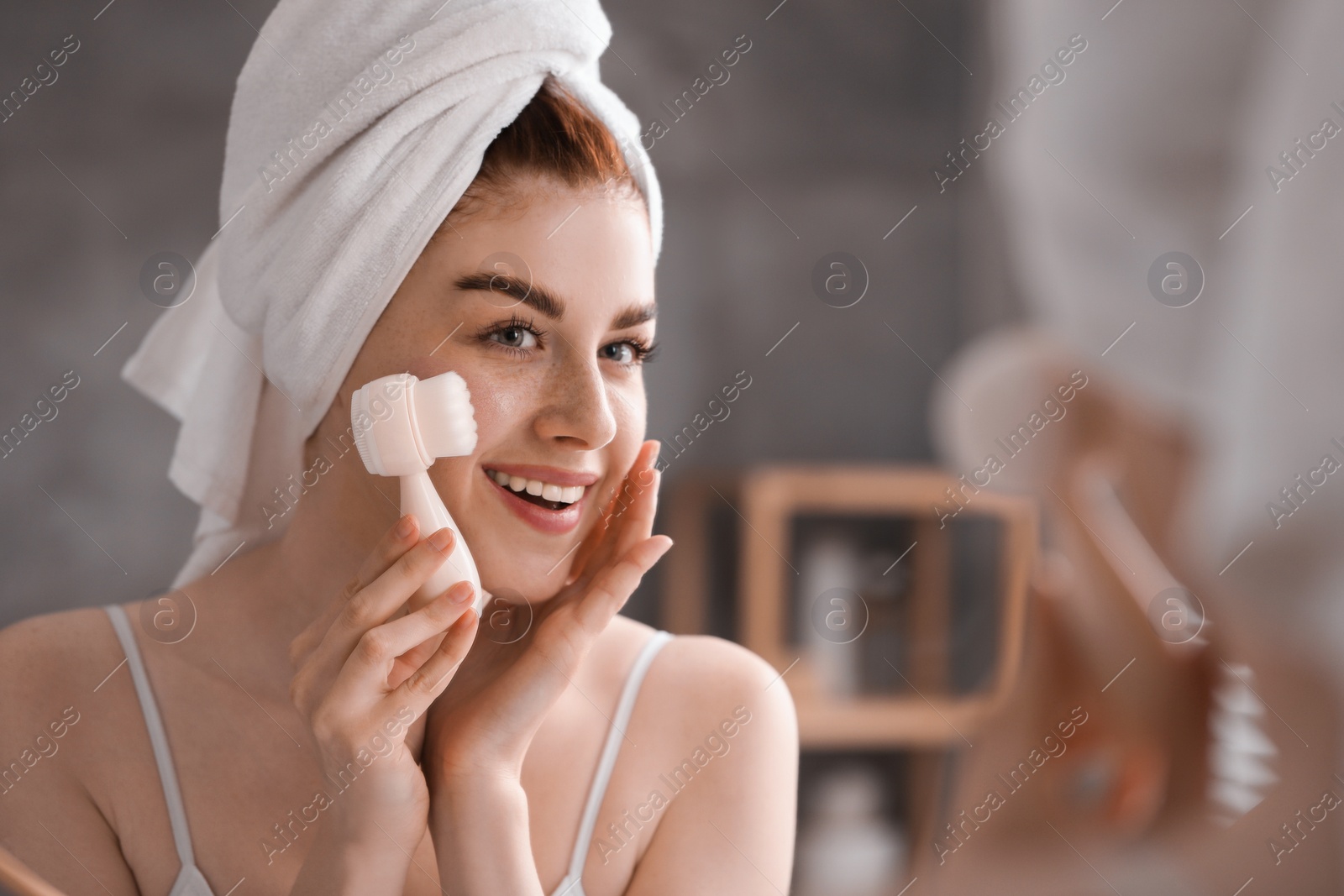 Photo of Washing face. Young woman with cleansing brush near mirror in bathroom