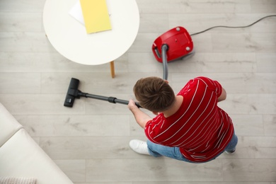 Young man using vacuum cleaner at home, top view