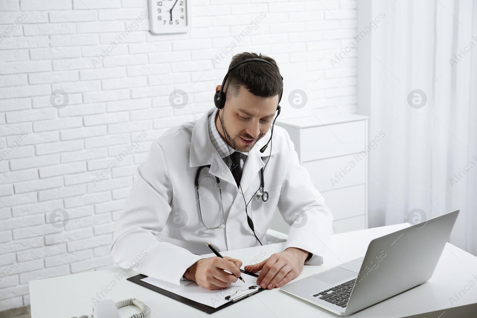 Photo of Doctor with headset consulting patient online at desk in clinic. Health service hotline