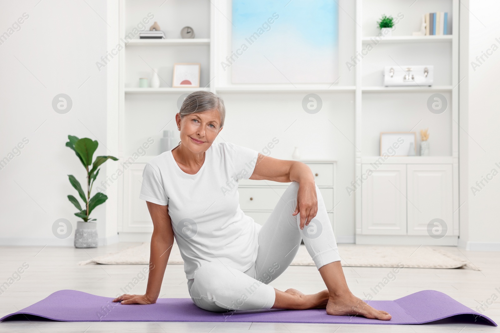 Photo of Happy senior woman sitting on mat at home. Yoga practice