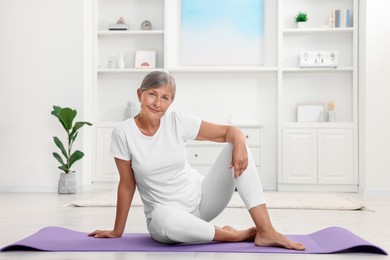 Happy senior woman sitting on mat at home. Yoga practice