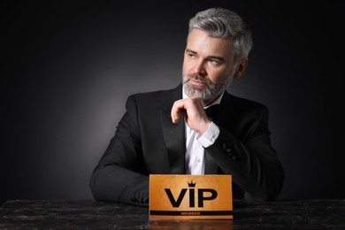 Photo of Handsome man sitting at table with VIP sign on black background