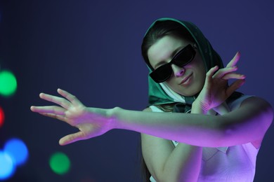 Photo of Portrait of beautiful young woman with sunglasses on color background with neon lights. Bokeh effect