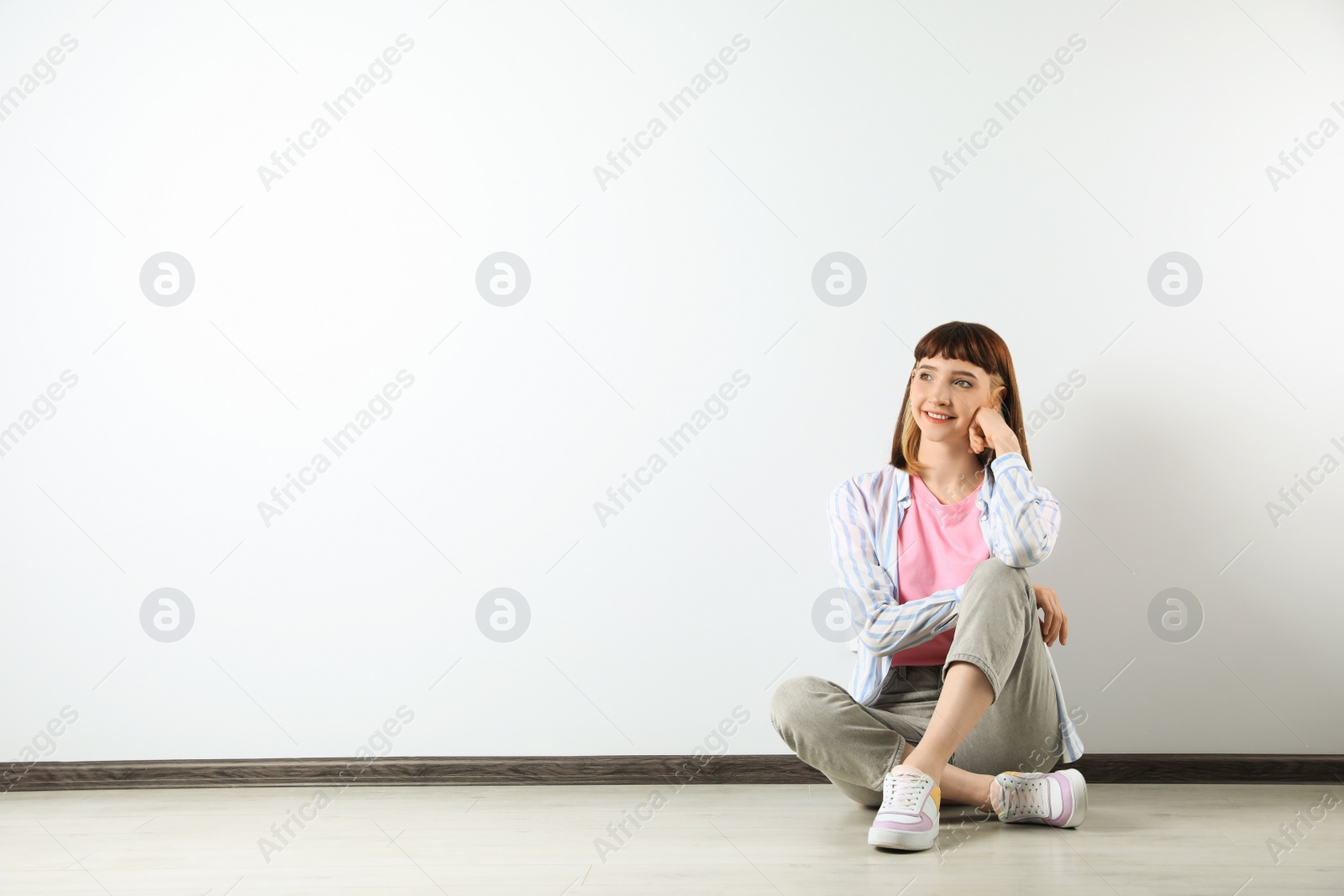 Photo of Beautiful young girl sitting on floor near white wall. Space for text