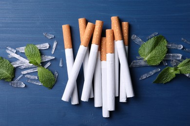 Photo of Cigarettes, menthol crystals and mint leaves on blue wooden table, flat lay