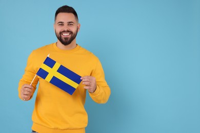 Young man holding flag of Sweden on light blue background, space for text