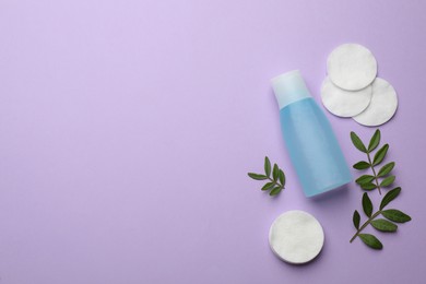 Photo of Cotton pads, leaves and makeup removal product on violet background, flat lay. Space for text