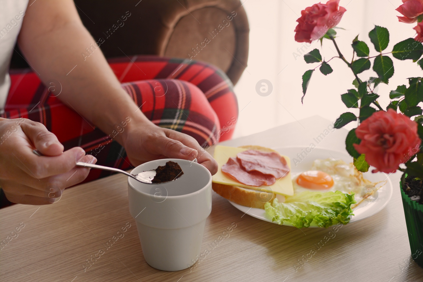 Photo of Woman making morning coffee while having breakfast at wooden table indoors, closeup