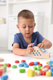 Photo of Motor skills development. Little boy playing with wooden lacing toy at white table indoors