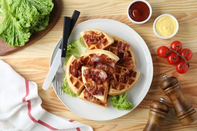 Tasty Belgian waffles served with bacon, lettuce and sauces on wooden table, flat lay