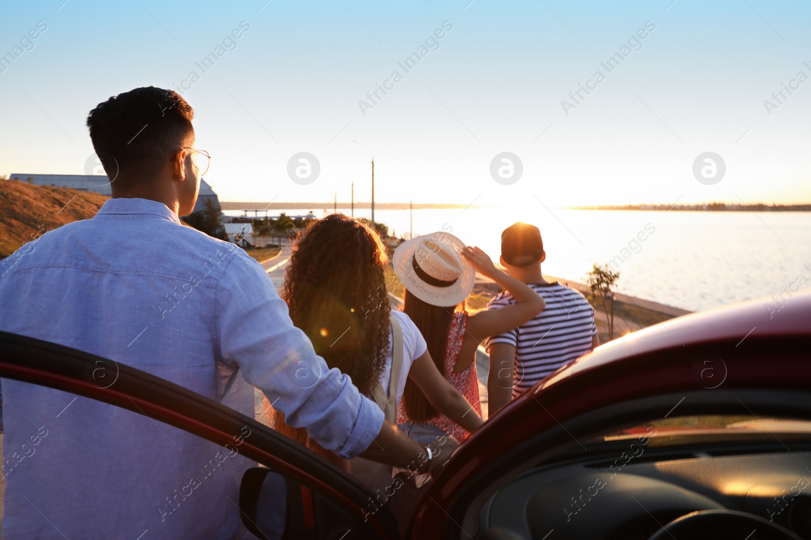 Photo of Group of friends near car outdoors at sunset, back view. Summer trip