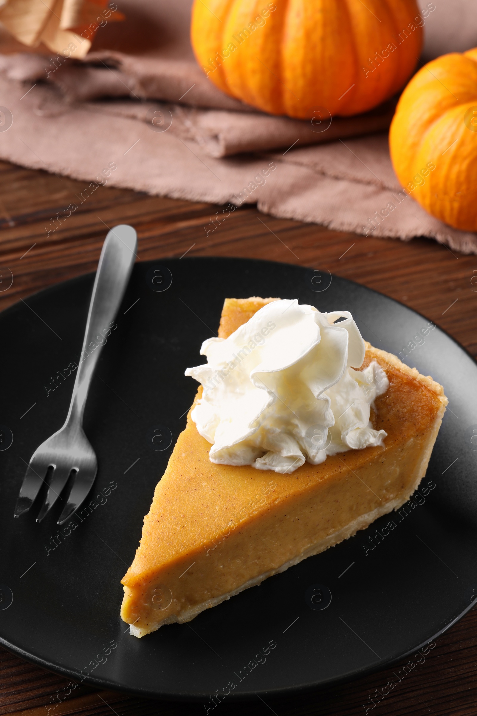 Photo of Piece of delicious pumpkin pie with whipped cream and fork on wooden table