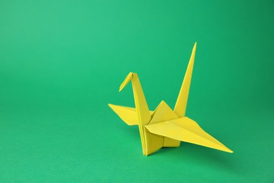 Photo of Paper origami crane on green background, space for text