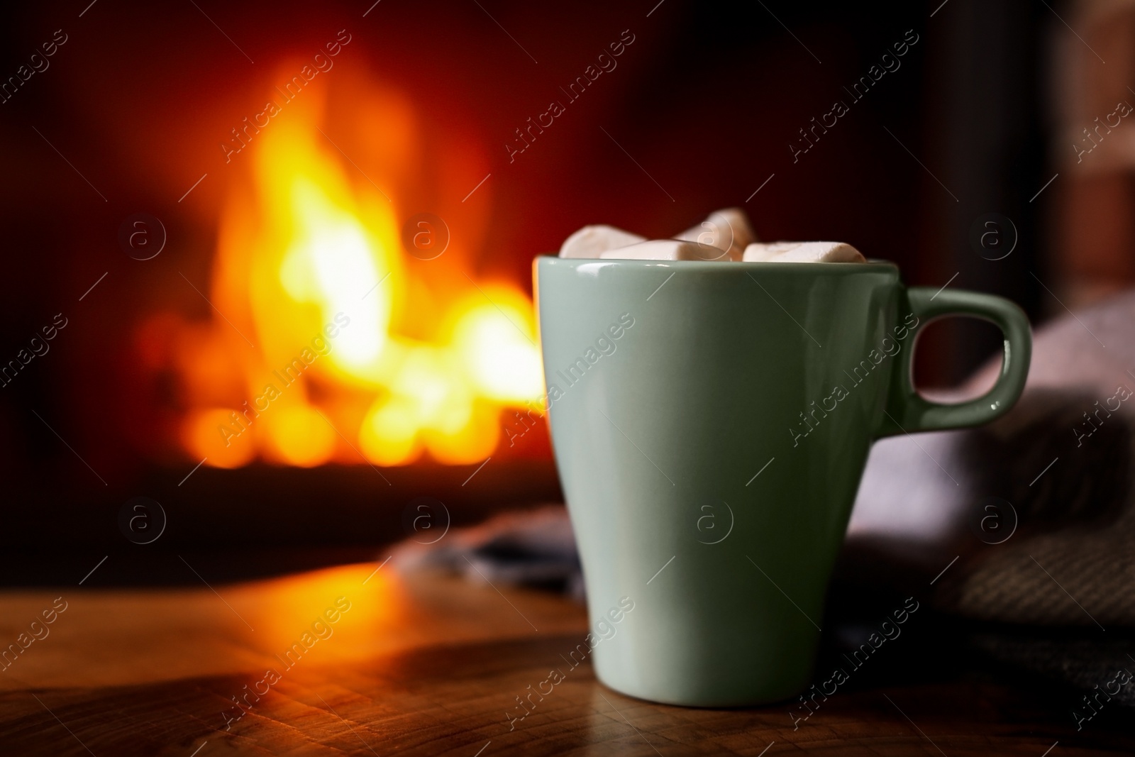 Photo of Delicious sweet cocoa with marshmallows and blurred fireplace on background