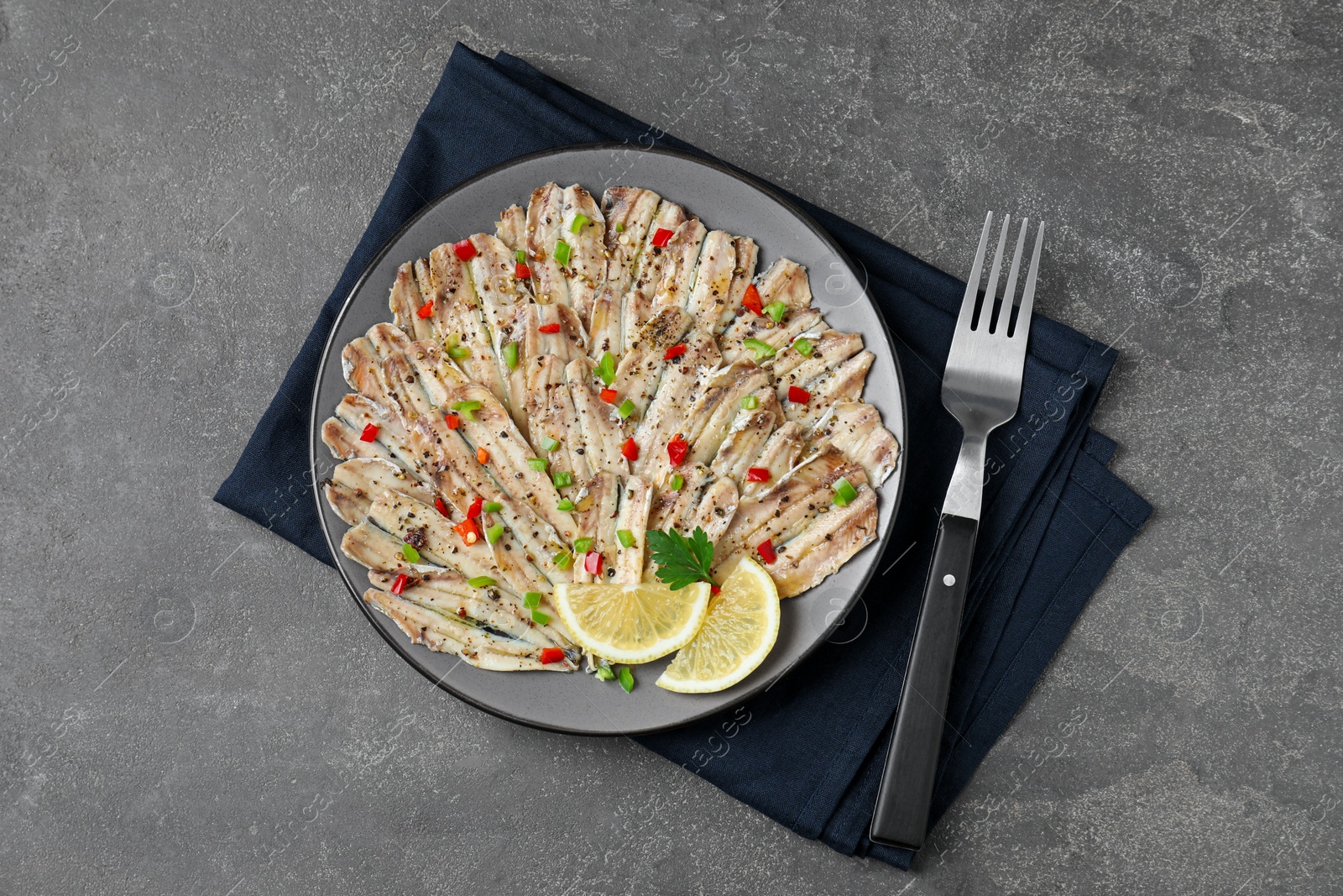 Photo of Tasty pickled anchovies with spices and fork on grey textured table, top view