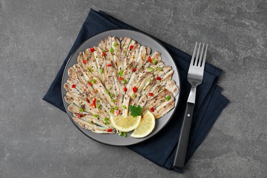 Photo of Tasty pickled anchovies with spices and fork on grey textured table, top view