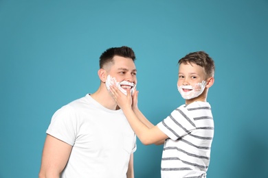 Son applying shaving foam on dad's face, color background