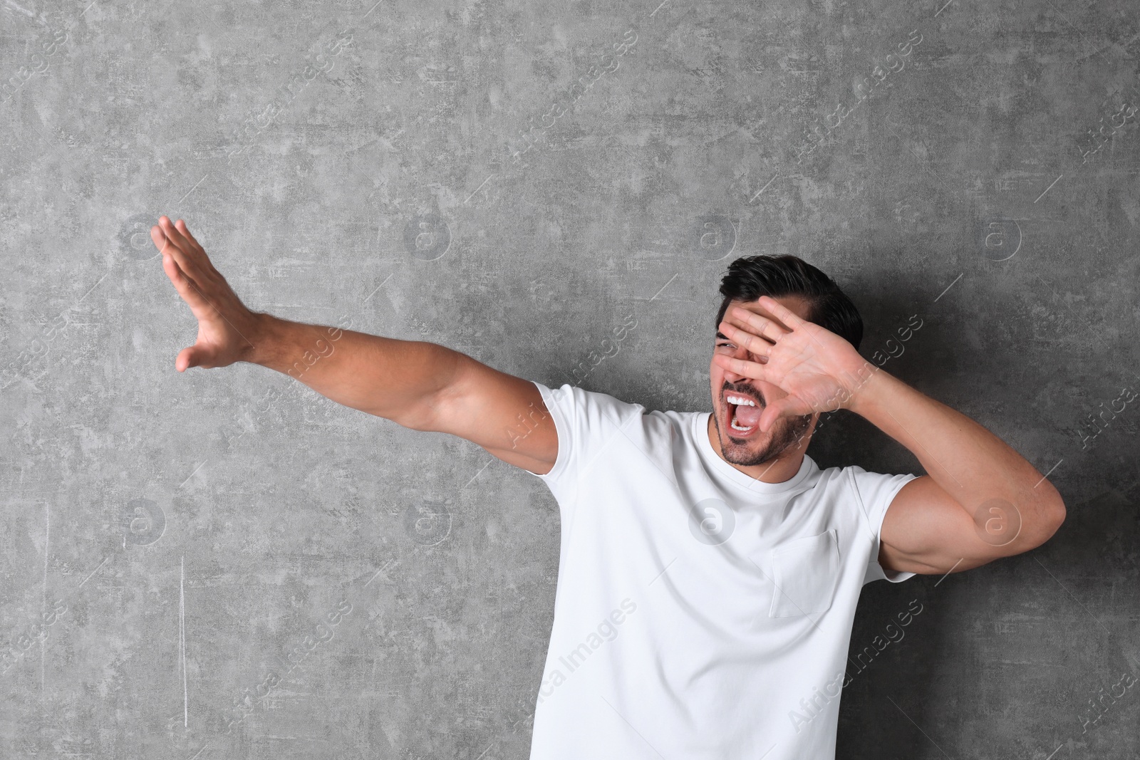 Photo of Young man being blinded and covering eyes with hand on grey background