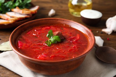 Stylish brown clay bowl with Ukrainian borsch served on wooden table, closeup