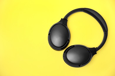 Modern wireless headphones on yellow background, top view. Space for text