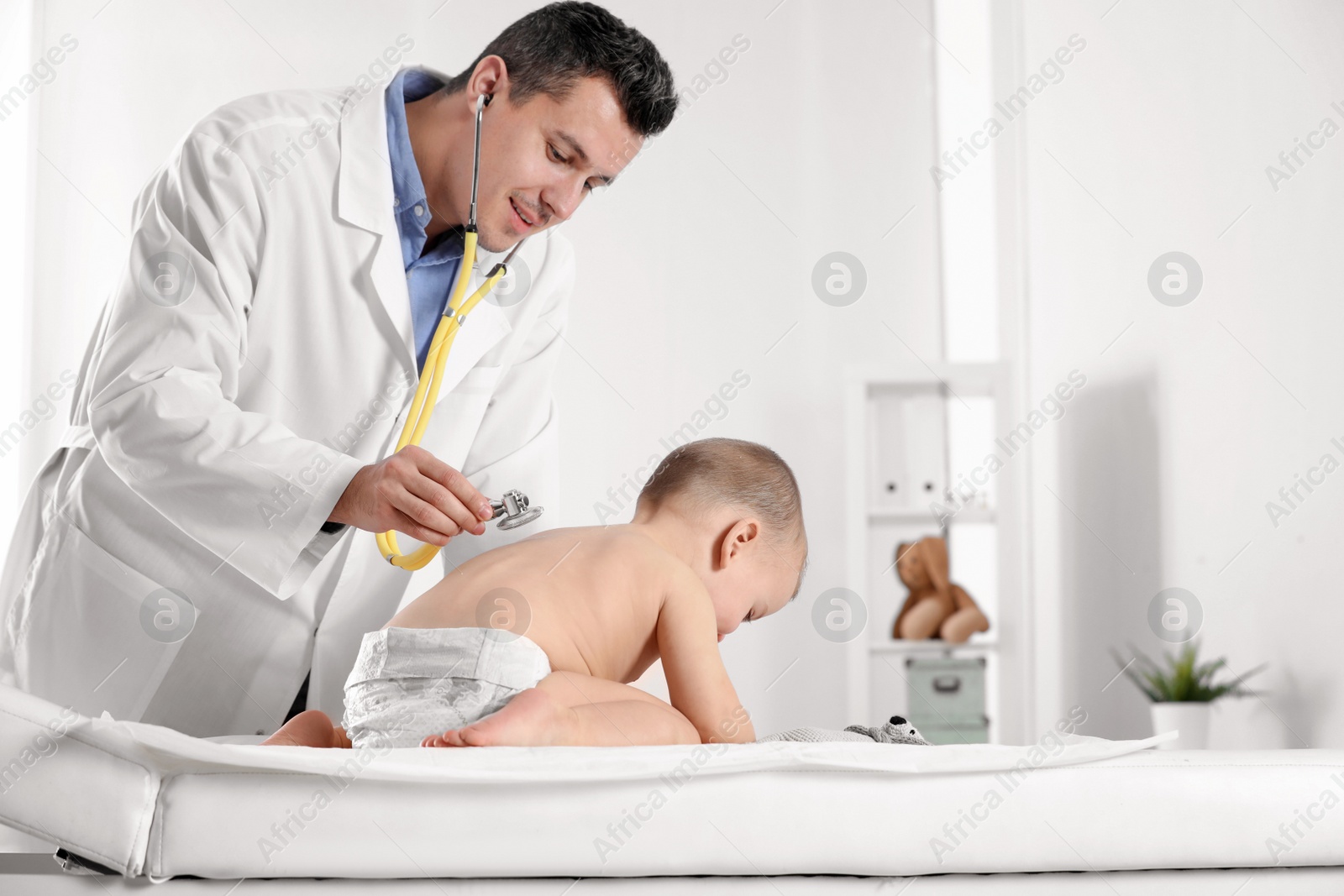 Photo of Children's doctor examining little boy with stethoscope in hospital. Space for text