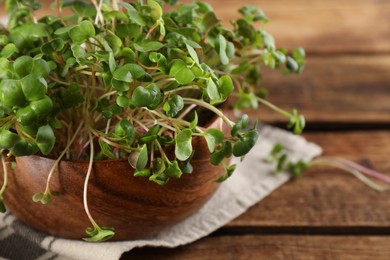 Fresh radish microgreens in bowl on wooden table, space for text