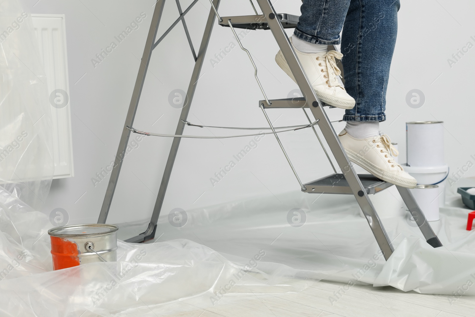 Photo of Woman climbing down metallic folding ladder near painting tools indoors, closeup