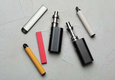Photo of Different electronic cigarettes on grey table, flat lay. Smoking alternative