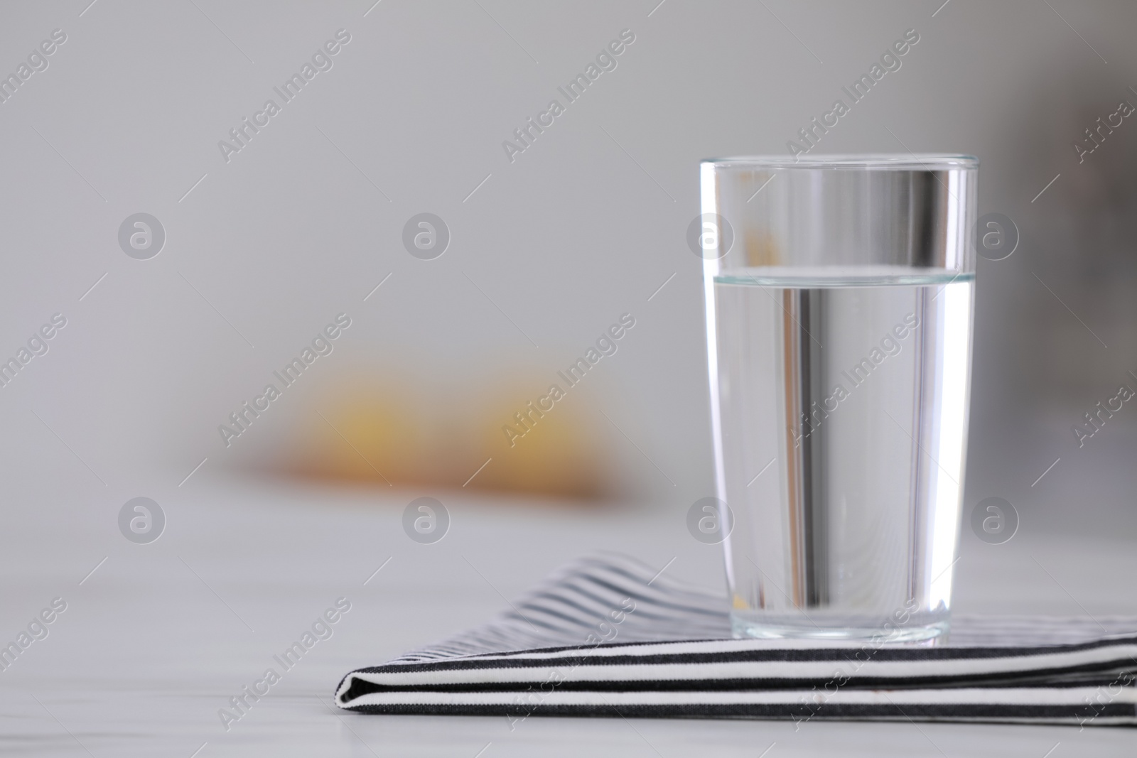 Photo of Glass of water and napkin on white table against blurred background. Space for text