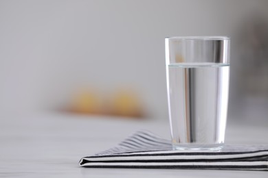 Photo of Glass of water and napkin on white table against blurred background. Space for text