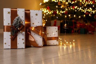 Photo of Beautiful gift boxes against fir tree with Christmas lights at home