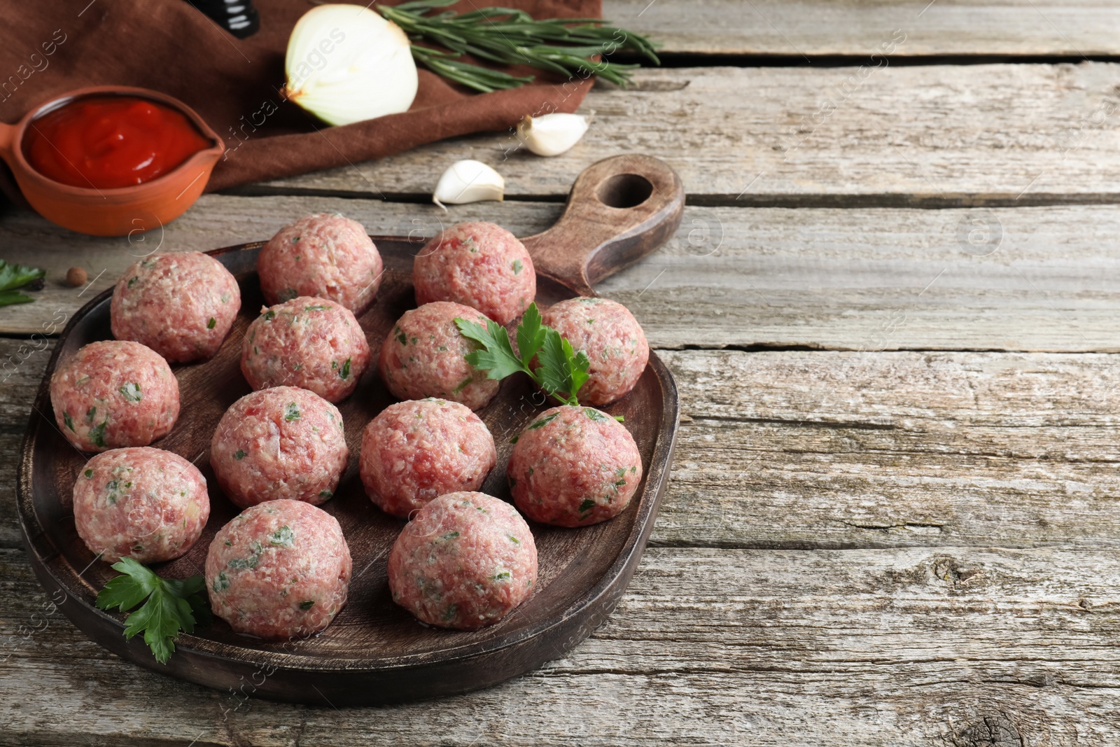 Photo of Many fresh raw meatballs and ingredients on wooden table, space for text