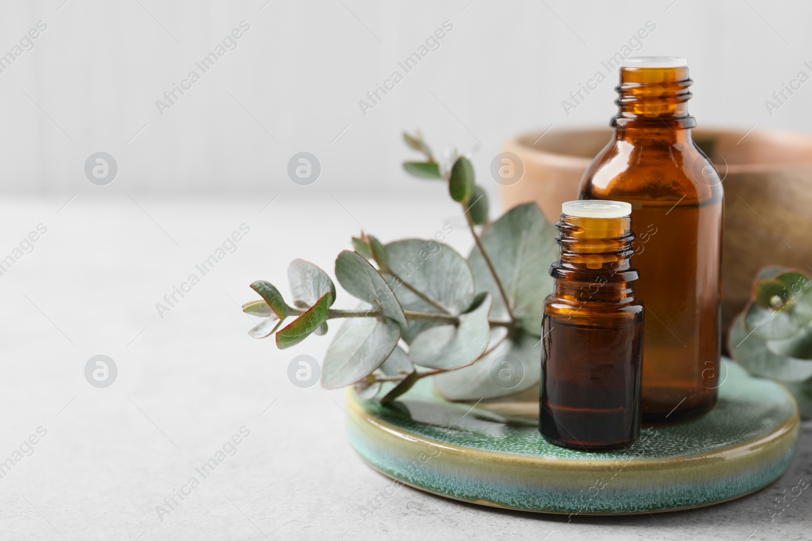 Photo of Bottles of eucalyptus essential oil and plant branches on white table, space for text