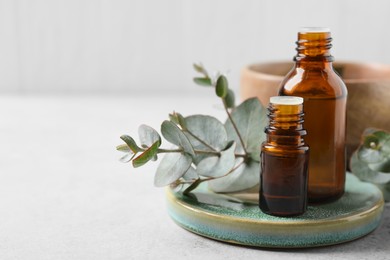 Photo of Bottles of eucalyptus essential oil and plant branches on white table, space for text