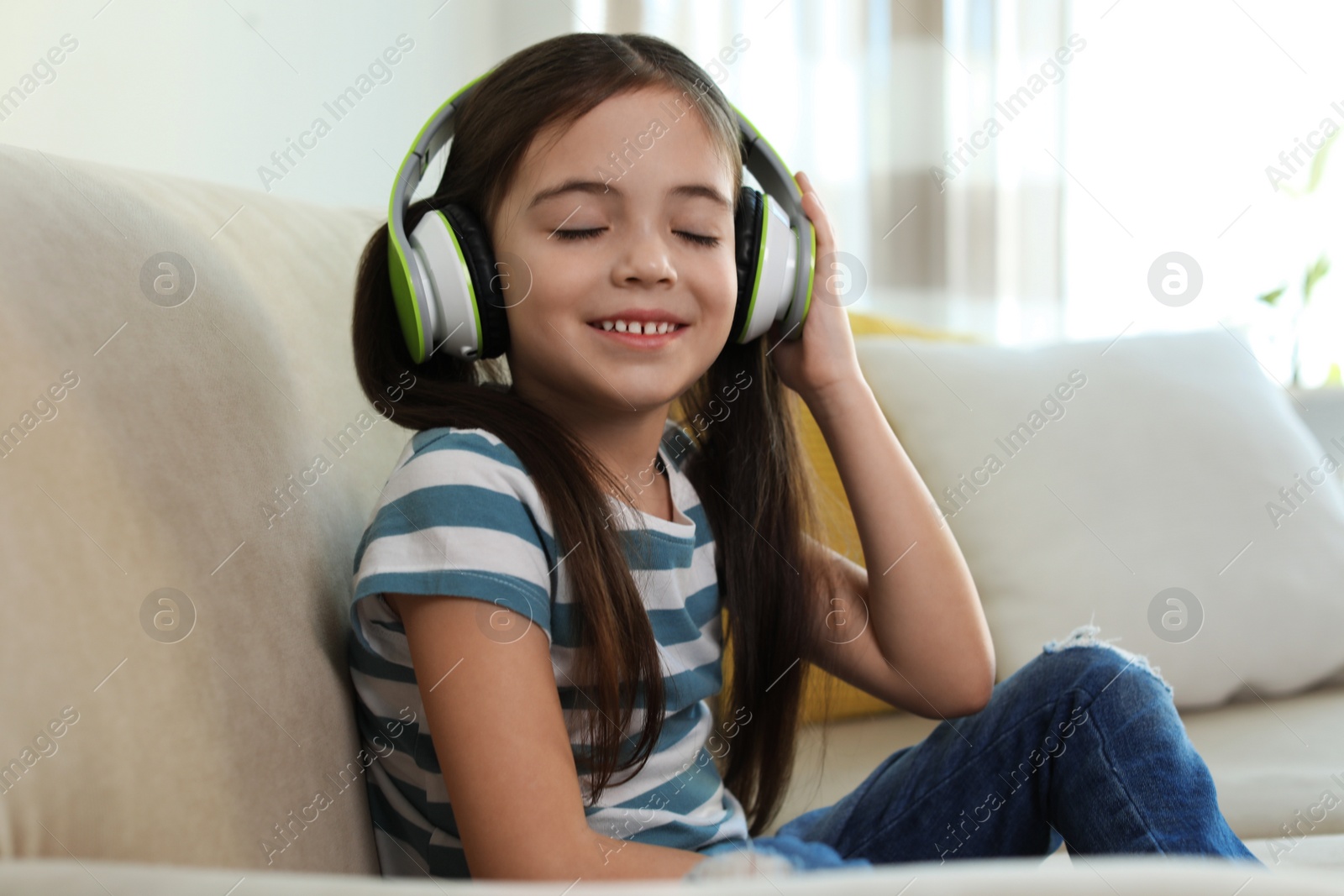 Photo of Cute little girl with headphones listening to audiobook at home