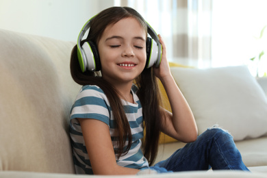 Photo of Cute little girl with headphones listening to audiobook at home