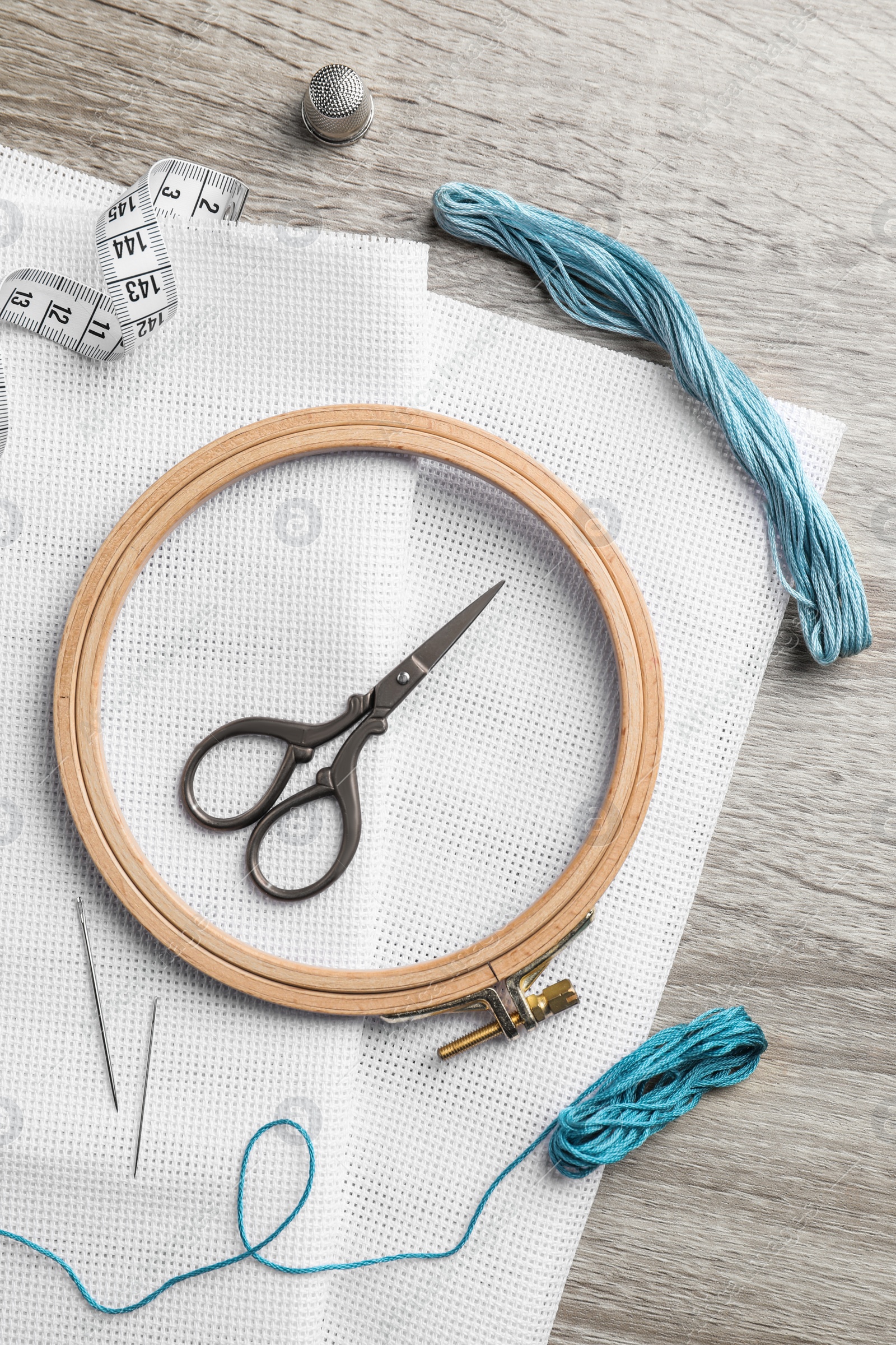 Photo of Embroidery hoop, fabric and other accessories on wooden table, flat lay